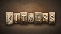 The word FITNESS is spelled out using old, rustic letterpress blocks against a dark, textured background. Each letter is distinct, showcasing a vintage and industrial style.