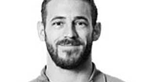 A man with short dark hair and a beard is wearing a collared shirt with the Kappa logo. The image is in black and white.