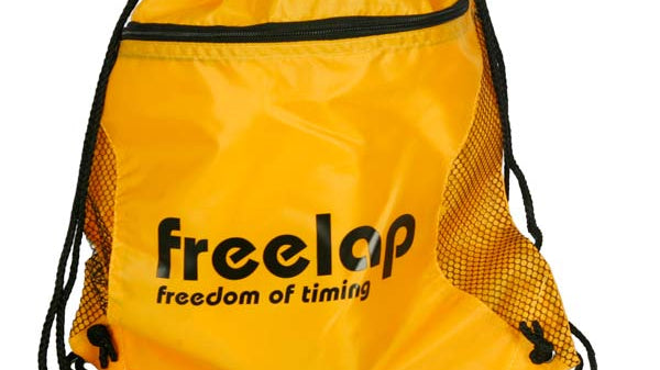 A yellow drawstring bag with black mesh sides and black cords. It has freelap and freedom of timing printed on the front in black letters.