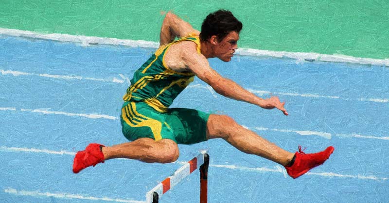 An athlete in a green and yellow uniform and red shoes leaps over a hurdle on a blue track.